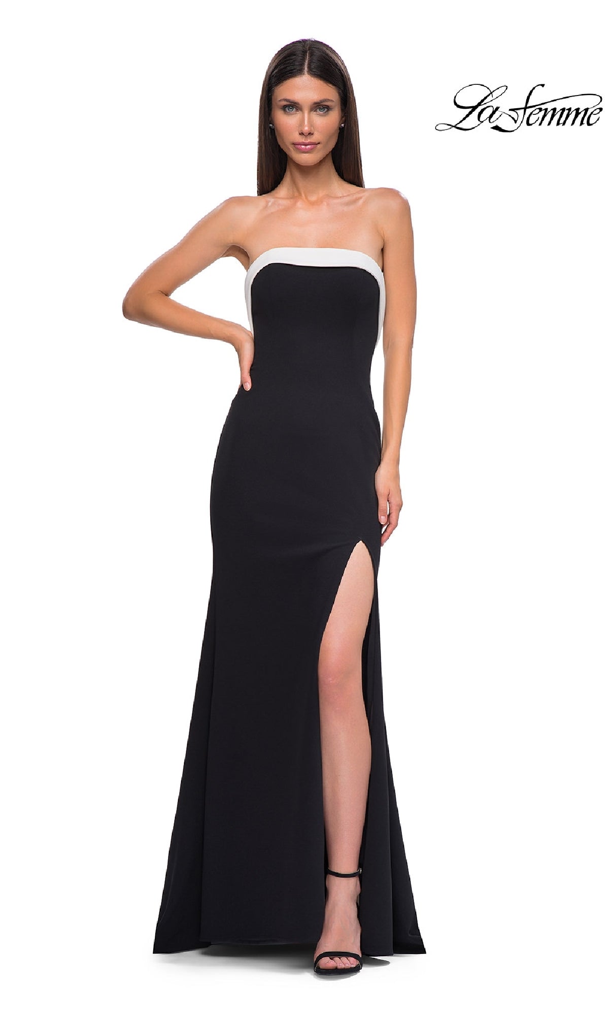 A woman poses confidently with one hand on her hip, wearing the La Femme 32808 strapless long black prom dress featuring a white trim, mermaid skirt, and high side slit. The